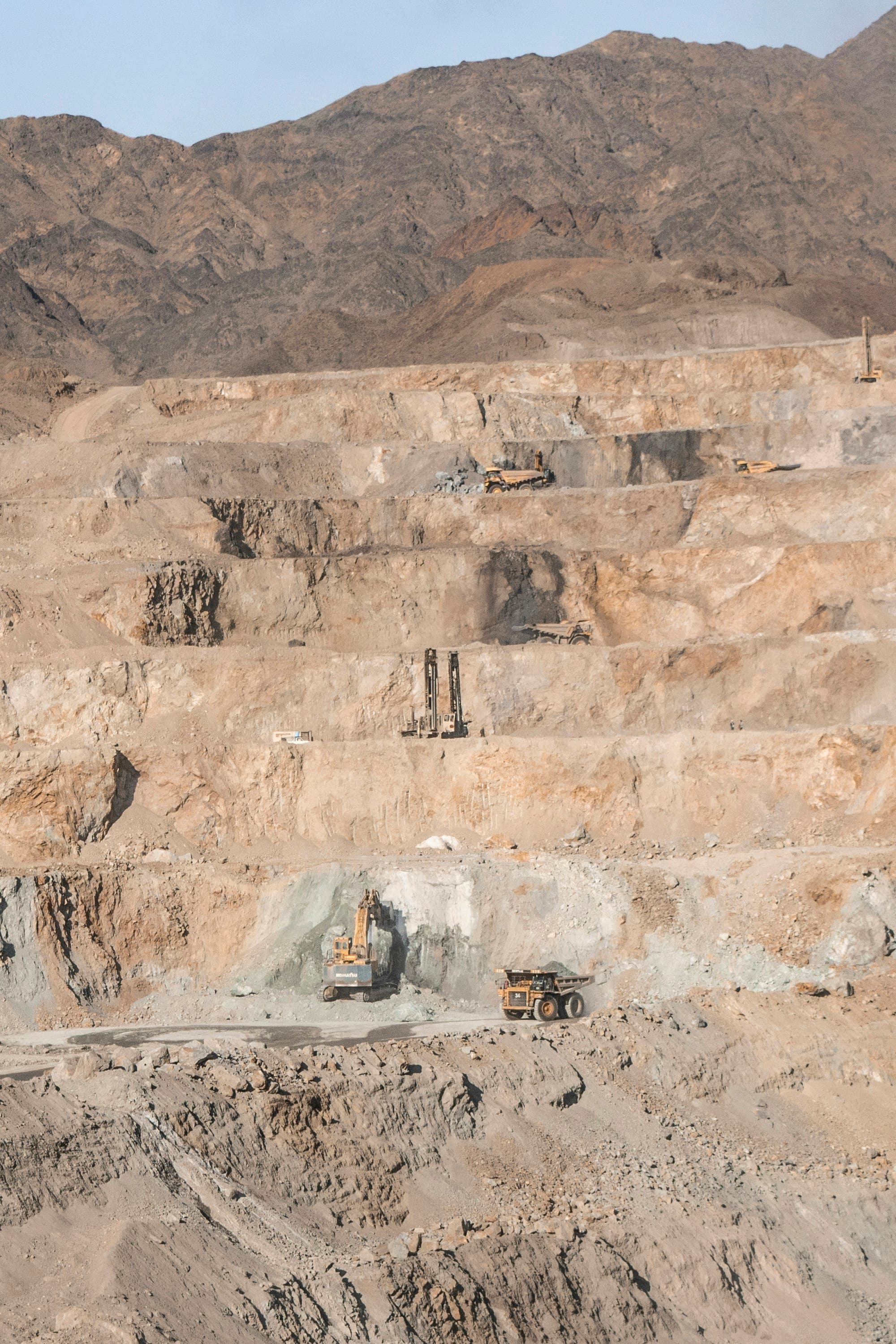 Benches of an open rock quarry, with a drill mast and haul trucks on the levels. This is not a photograph of the SPR quarry.