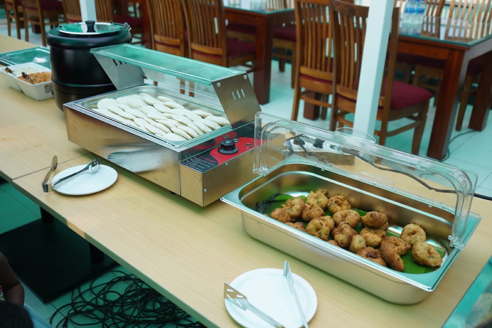 Idli in a warmer and vada in a tray, set out in the dining hall. Published on the resort sites.